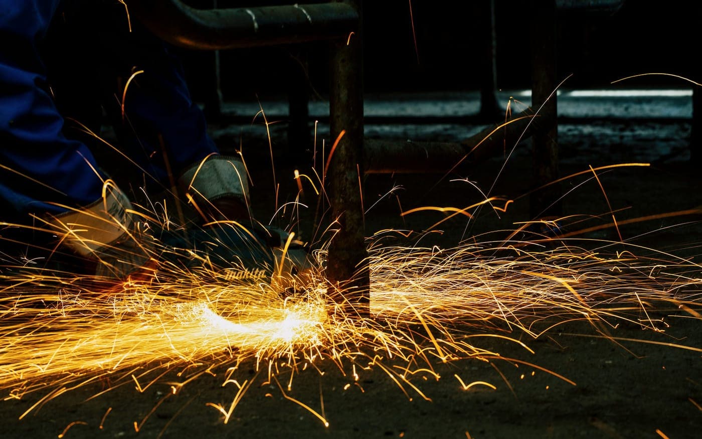 Sparks flying from an angle grinder cutting steel section in a fabrication workshop