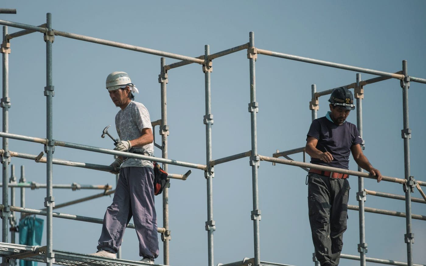 Two scaffolders assembling a modular cuplock scaffold frame against a clear sky