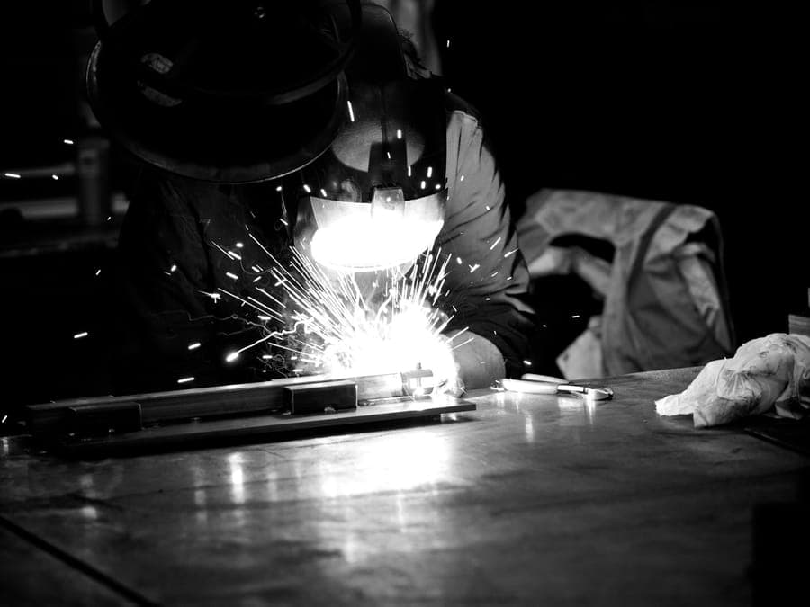 Welder joining steel on a workbench, sparks lighting the workshop